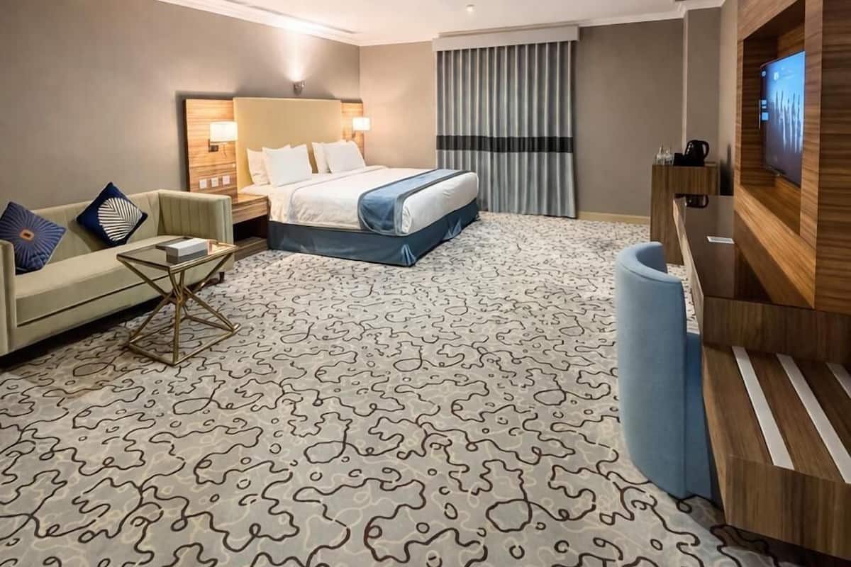 A hotel room with a bed, a sofa, a TV, and a patterned carpet.