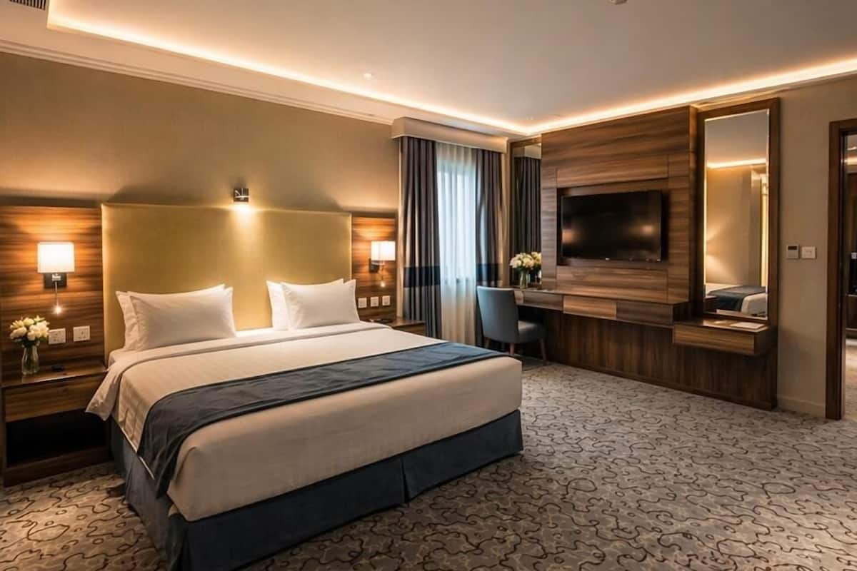 A modern hotel room with a large bed, a desk, a flat-screen TV, and a mirror.