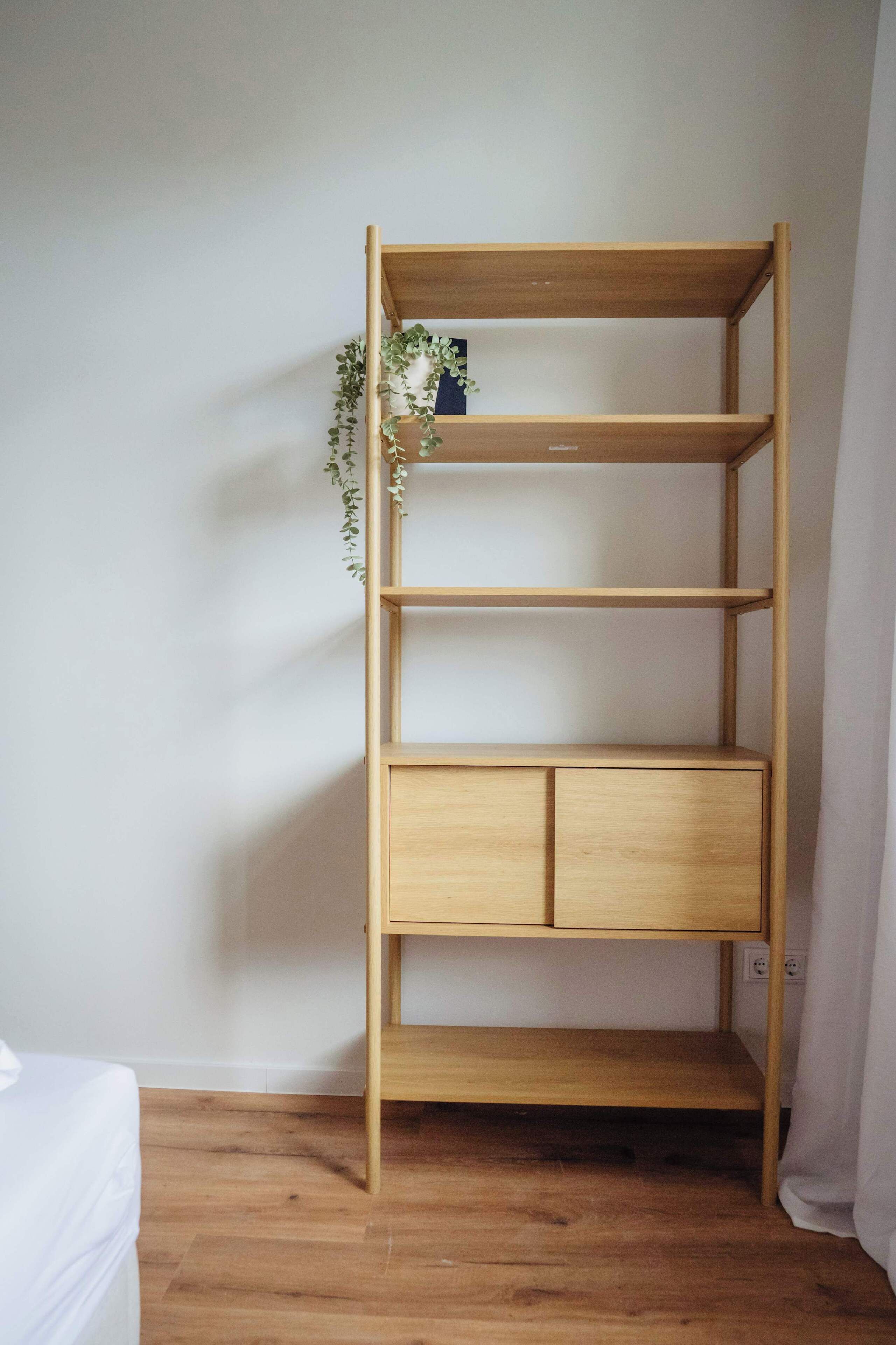 Ein Holzbücherregal mit drei Einlegeböcken und einem Unterschrank, vor einer schlichten Wand und einem Holzboden.