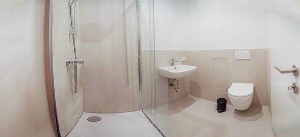 Un baño moderno con ducha de vidrio, lavamanos blanco y retrete.