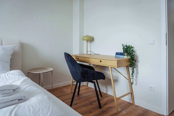 Un dormitorio con cama, escritorio, silla, lámpara y una pequeña planta en maceta.