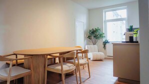 Ein stilvoller Essbereich mit Holztisch und -stühlen, einem weißen Sofa und einem Blumentopf in der Nähe eines Fensters.