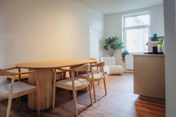 A modern dining area with a wooden table and chairs, a white sofa, and a potted plant by a window.
