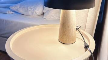A bedside table with a lamp, a bed, and a window with curtains.