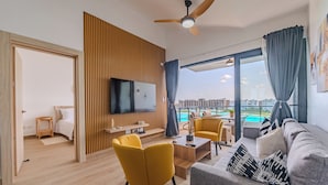 Un salon moderne doté d’un téléviseur à écran plat, de fauteuils jaunes, d’un canapé gris et d’une grande fenêtre offrant une vue sur des immeubles et une piscine.