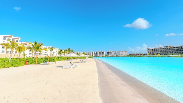 Un complexe hôtelier de bord de mer avec un ciel bleu azur, une plage de sable et une grande piscine.