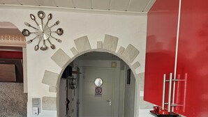 Une cuisine avec une casserole rouge posée sur le comptoir, une horloge au mur et un panneau « interdiction de fumer » au-dessus de la porte.