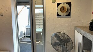 Une chambre d’hôtel avec un lit, une porte vitrée donnant sur l’extérieur, une horloge murale et un ventilateur sur pied.