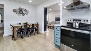 Une cuisine moderne avec un coin repas, comprenant une table et des chaises en bois, une cuisinière en acier inoxydable et un élément décoratif mural.