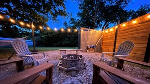 Un espace extérieur aménagé avec des chaises Adirondack, un foyer et des guirlandes lumineuses.