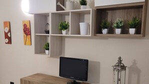 Ein modernes Wohnzimmer mit einer Holz-Unterhaltungsecke, einem Flachbildfernseher und dekorativen Regalen mit Pflanzen und Vasen.