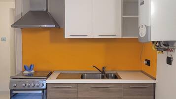 A compact kitchen with a stove, sink, and white cabinets.