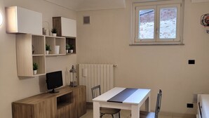 Ein kompakter Wohnbereich mit Esstisch, Stühlen, einem Fernseher auf einer Holzkommode und einer Heizung.
