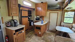A compact RV kitchen with wooden cabinets, a built-in oven, and a small dining area. - A&J Country RV Getaway (Gilman)