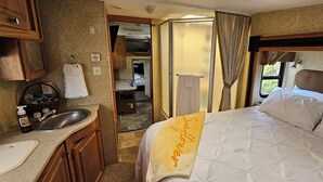 A compact RV interior with a kitchenette, a bed with a towel, and a bathroom. - A&J Country RV Getaway (Gilman)