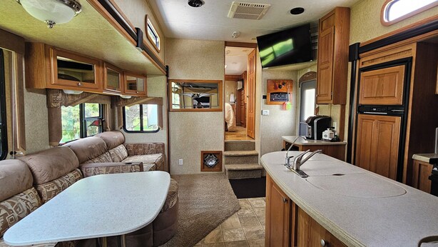 A compact RV interior with a kitchenette, a dining area, and a living space with a sofa and table. - A&J Country RV Getaway (Gilman)