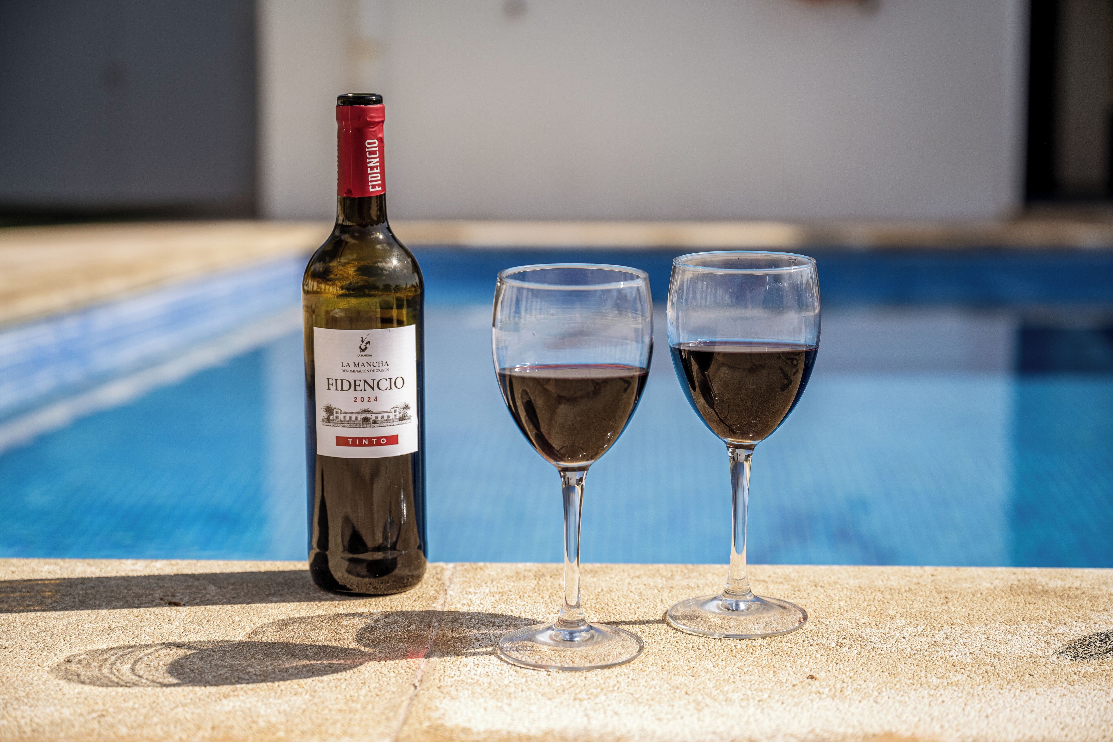 A bottle of wine and two glasses on a poolside.