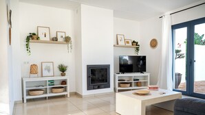 A modern living room with a fireplace, TV, and white furniture. - Elegant and modern detached villa with swimming pool (Santanyí)