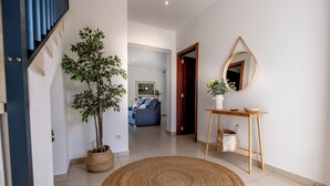 A hallway with a woven rug, a potted plant, a wooden console table with a mirror, and a blue sofa in the background. - Elegant and modern detached villa with swimming pool (Santanyí)