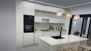 A modern kitchen with white cabinetry, a black oven, a large island with stools, and pendant lights.