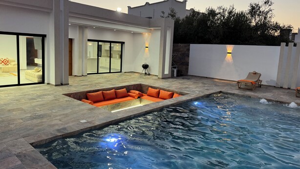 A modern outdoor pool area with a built-in seating area and a view of the house.