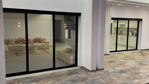 A modern house with a spacious patio area featuring a stone floor and a large sliding glass door leading to an interior with a sofa and a dining area.