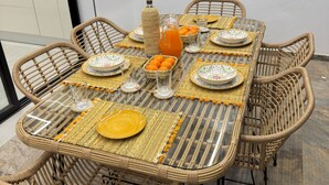 A dining table set with wicker chairs, a pitcher of orange juice, and decorative plates.
