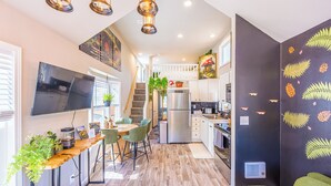 Una cocina moderna con un refrigerador grande, una zona de comedor con una mesa de madera y sillas verdes, y una escalera que conduce a un nivel superior.