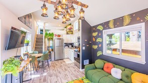 Una cocina moderna con una isla central, una zona de comedor con un sofá verde y una escalera que lleva a un nivel superior.