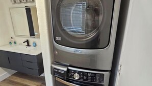 A compact, wall-mounted washer and dryer unit with a control panel, located in a modern kitchen with a wooden floor and a built-in sink.