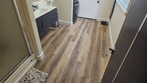 A narrow hallway with a wooden floor, a small bathroom with a sink and mirror, and a refrigerator.