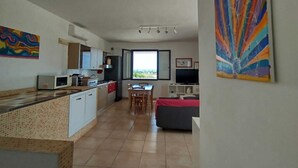 Een moderne keuken met witte kasten, een magnetron en een fornuis. Er is een eethoek met een tafel en stoelen, en een groot raam met uitzicht.