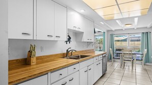 Eine moderne Küche mit weißen Schränken, einer Holzauskładung und einem Spülbecken. Es gibt einen Essbereich mit Tisch und Stühlen.