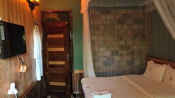 A room with a wooden door, a bed with white bedding, a TV mounted on the wall, and a brick wall.