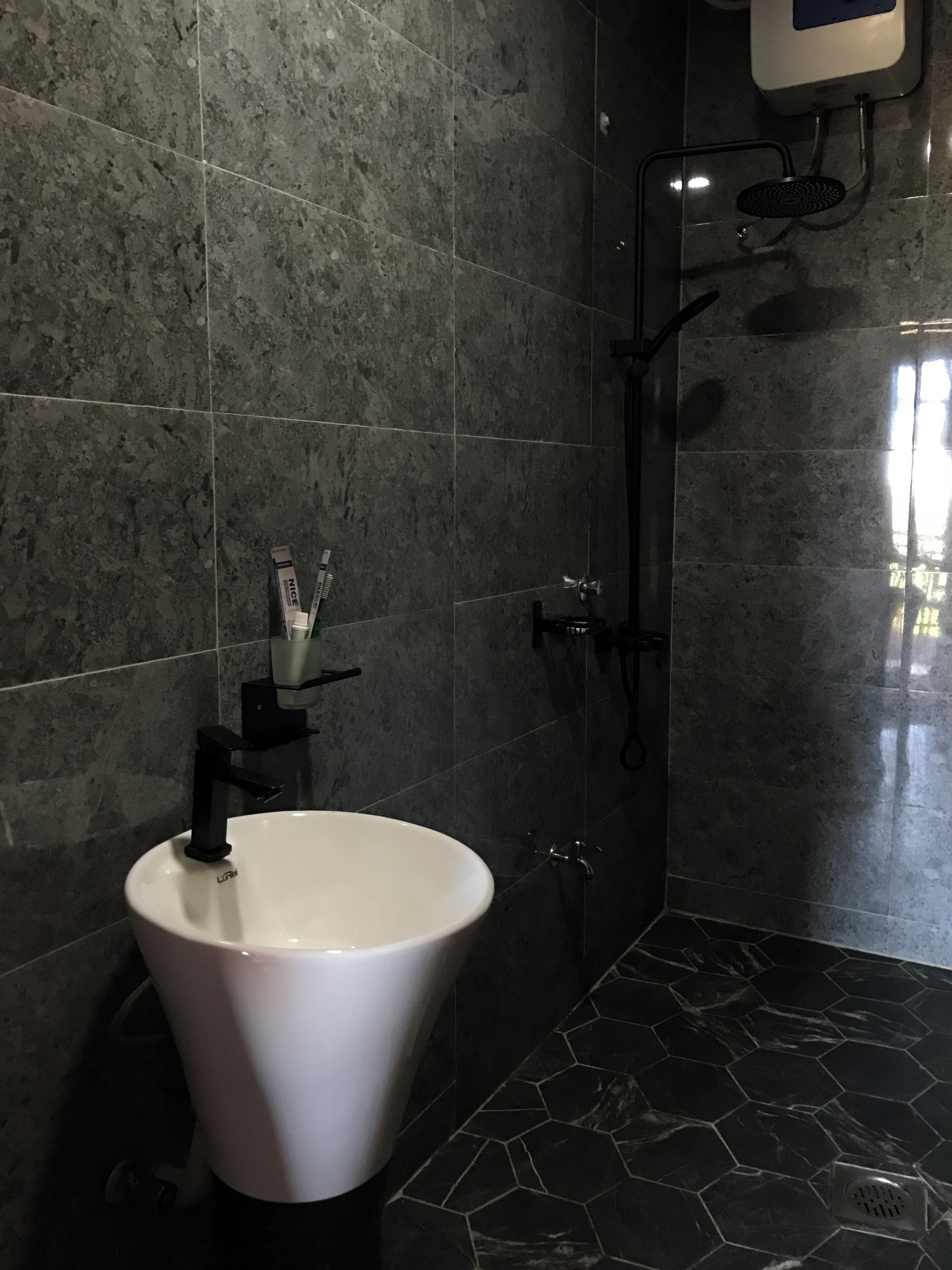Une salle de bain avec des carreaux de marbre foncé, un lavabo blanc et un espace douche.