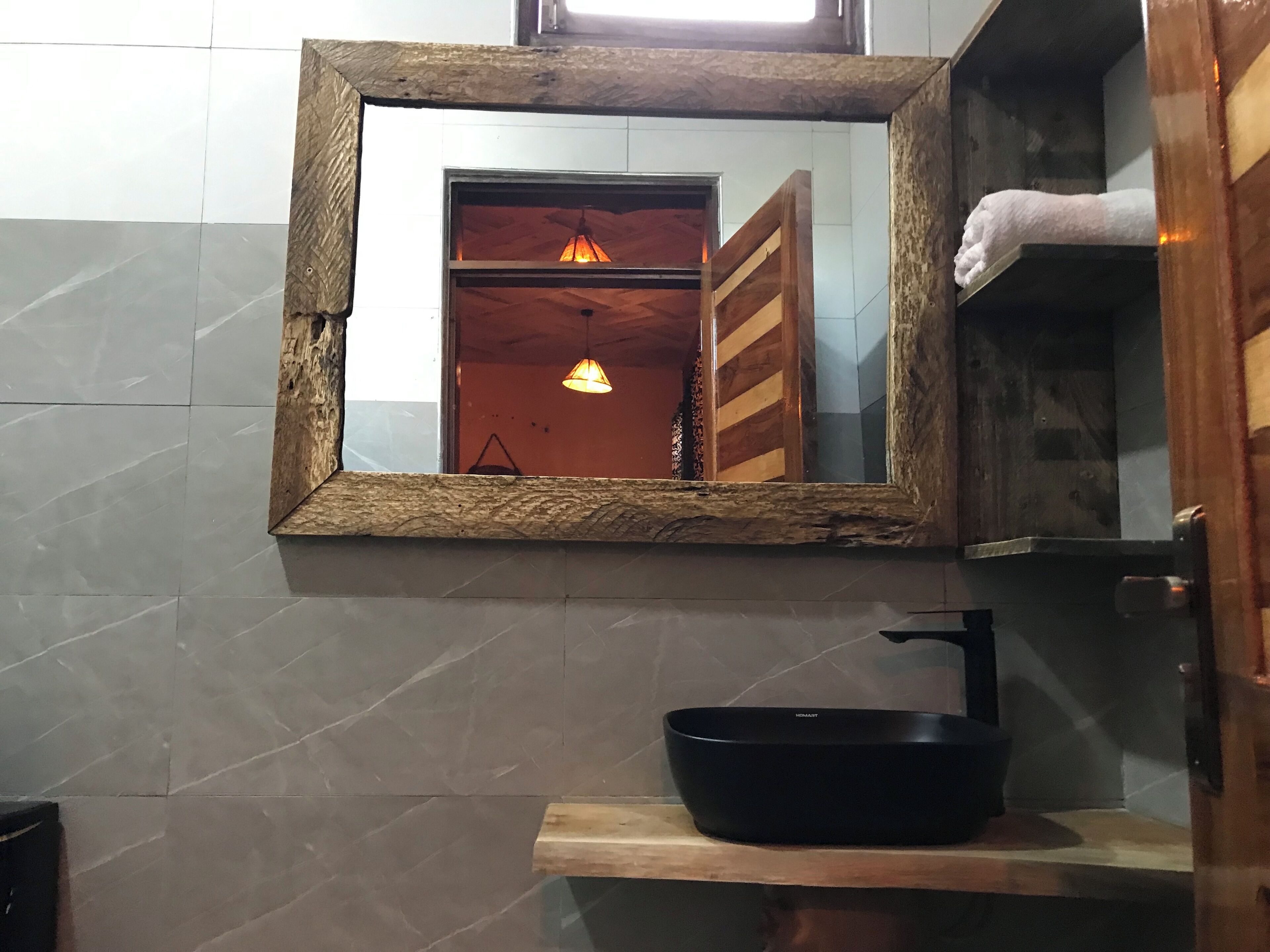 Un baño con espejo de marco de madera, lavabo negro y un perchero para toallas.