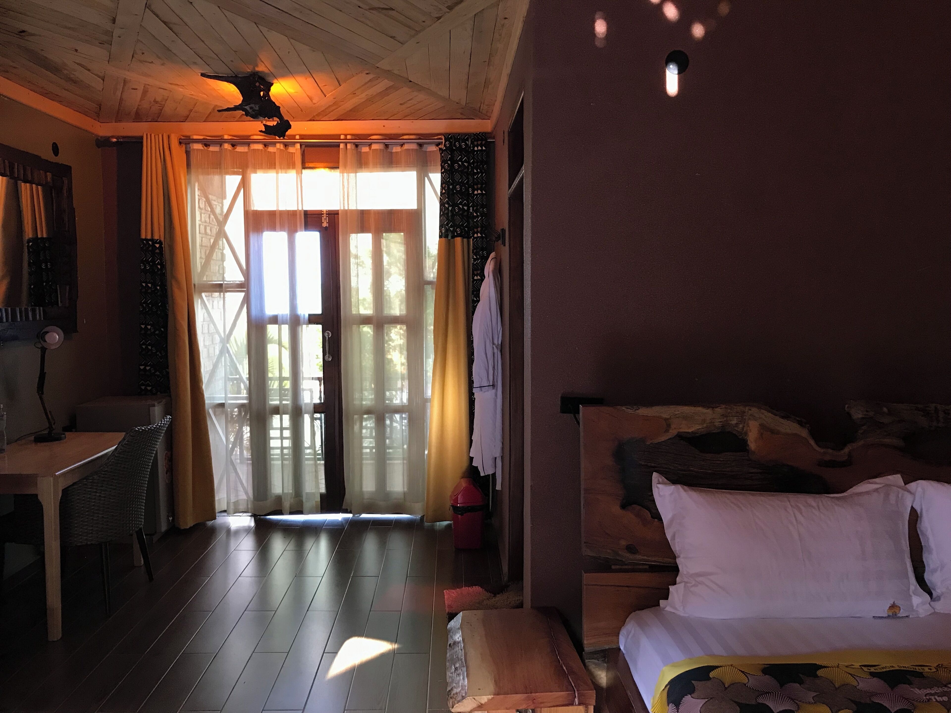 A cozy room with a bed, a desk, and a chair. There is a window with curtains and a view outside.