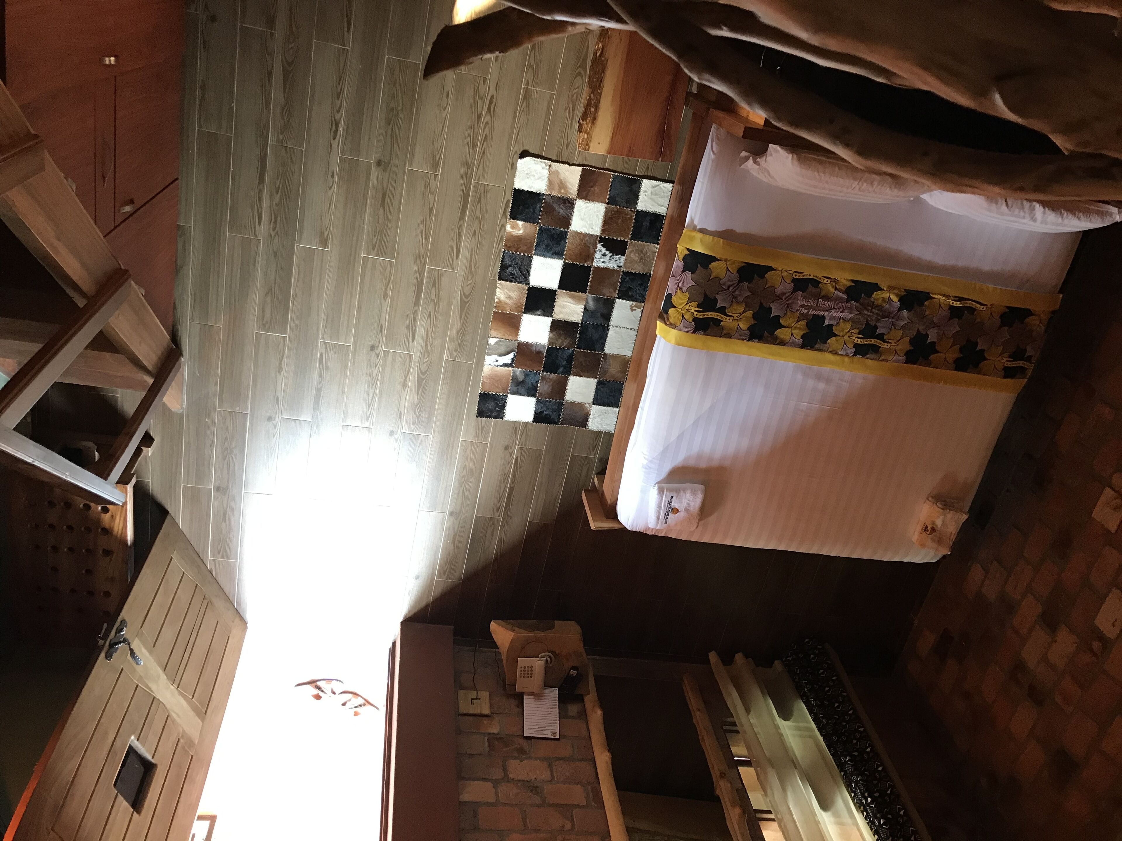 Una habitación con una cama, un tapete de cuadros, suelo de madera y pared de ladrillo.