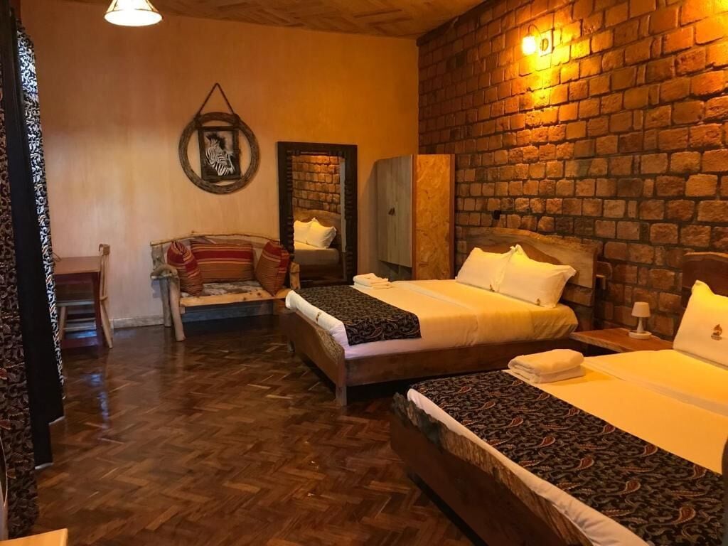 A cozy room with two beds, a wooden floor, a brick wall, and a mirror.