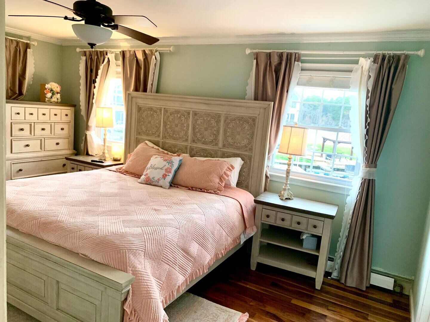 Een slaapkamer met een groot bed, een nachtkastje, een dressoir en een raam met gordijnen.