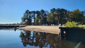 A calm lake with a dock, surrounded by tall trees and a clear blue sky.