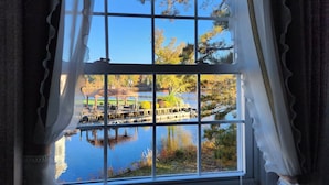 A window with a view of a dock and a body of water, surrounded by trees with autumn foliage.