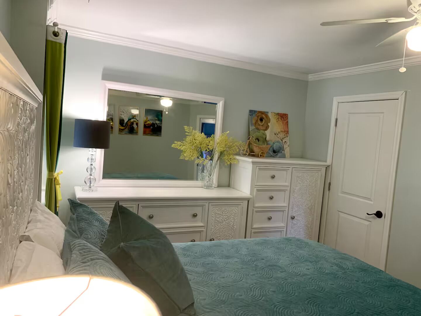 Un dormitorio con cama, cómoda, espejo y cuadros en la pared.