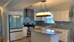 A modern kitchen with white cabinetry, a granite countertop island, and a stainless steel range hood.