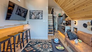 Una cocina moderna con armarios de madera, un comedor con un banco de madera y una sala de estar con sofá y mesa de centro.