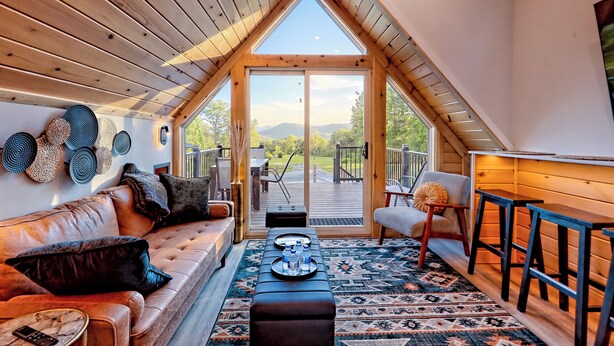Un dormitorio tipo loft acogedor con techo inclinado, un ventanal grande, techo de madera, un sofá, una mesita de centro y vistas al exterior.