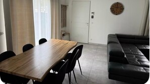 A living room with a black leather sofa, a wooden dining table with chairs, and a white door with a clock on the wall. - House with swimming pool in Provence near la sainte victoire (Fuveau)