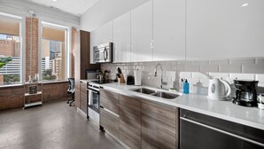 A modern kitchen with white cabinets, stainless steel appliances, and a large window offering a city view. - Prime Downtown Dallas | Pool + Theater + Game Room (Dallas)