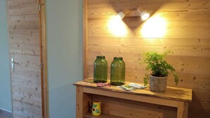 Eine hölzerne Bank mit Ablage, zwei grüne Glasflaschen, ein Blumentopf und eine Lampe.