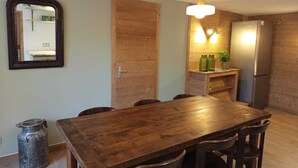 Ein Holztisch mit Stühlen, eine Holztür, ein Kühlschrank und Pendelleuchten.